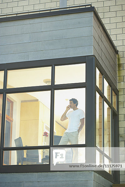 Mann telefoniert mit Handy neben dem Fenster