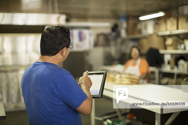 Hispanischer Bäcker mit Tablet-Computer in der Küche