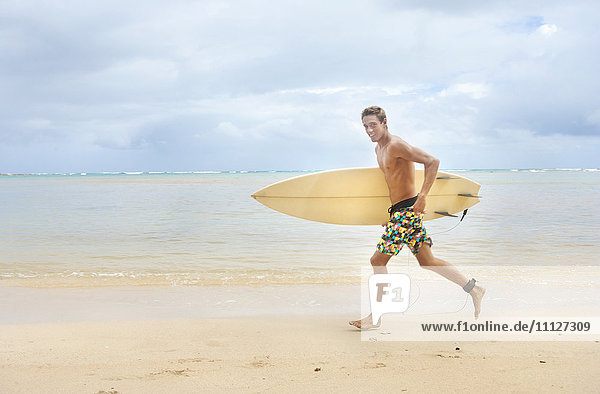 Caucasian man running on beach carrying surfboard