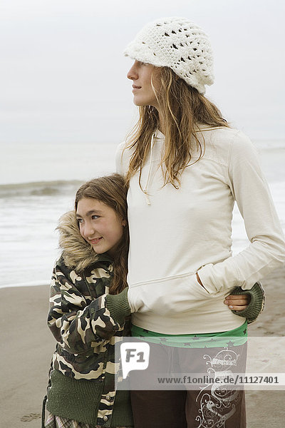 Gemischtrassige Frau und Schwester umarmen sich am Strand