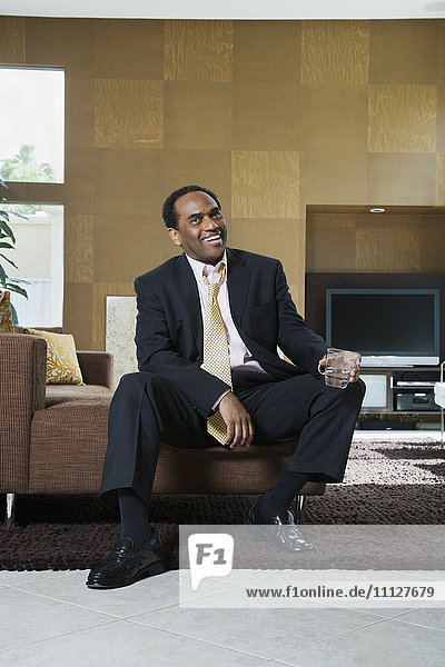 Afrikanischer Geschäftsmann sitzt in einem modernen Wohnzimmer mit einem Getränk