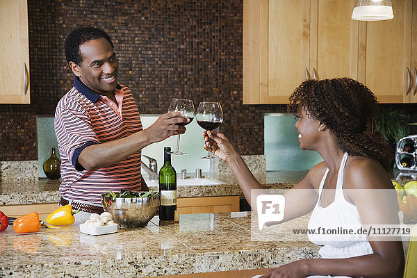 Afrikanisches Paar stößt in der Küche mit Rotwein an