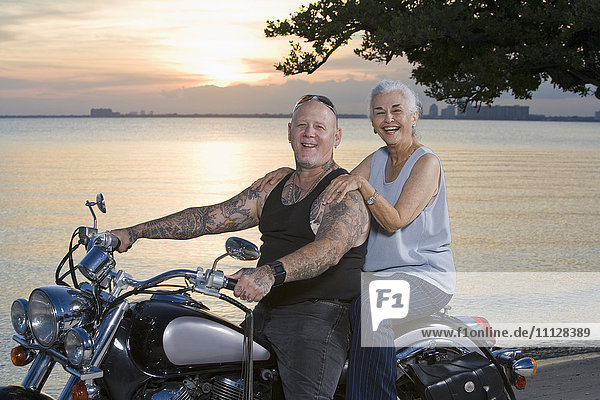 Mother and tattooed son riding motorcycle at the beach