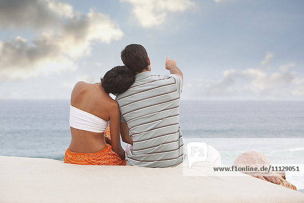 Hispanisches Paar sitzt und schaut aufs Meer
