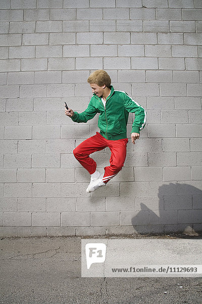 Mixed race boy jumping in mid-air using cell phone