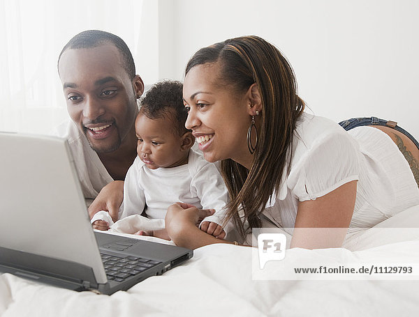 Afrikanisches Paar und Baby mit Laptop auf dem Bett