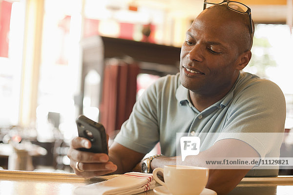 Afroamerikanischer Mann in einem Restaurant  der eine SMS auf seinem Mobiltelefon schreibt