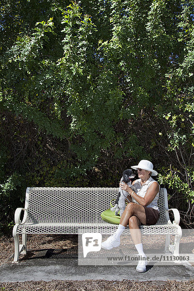 Kaukasische Frau sitzt mit Hund auf einer Parkbank