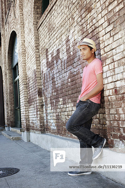 Asian man leaning against brick wall