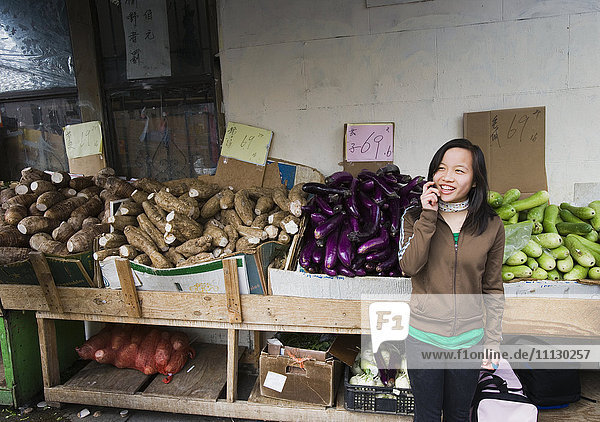 Chinesisches Mädchen  das auf einem Markt im Freien mit einem Handy telefoniert