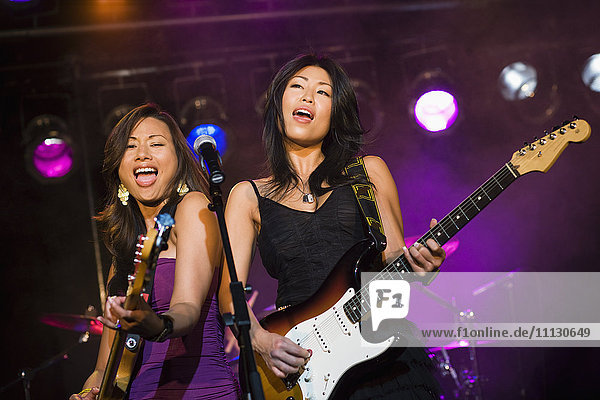 Asian women singing and playing electric guitar onstage