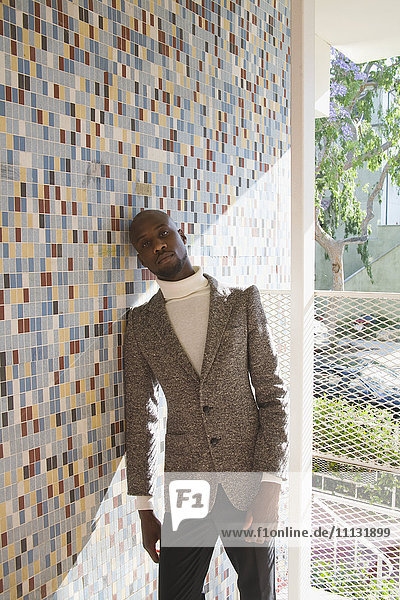 African man in tweed jacket leaning against tiled wall