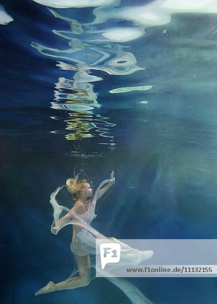 Kaukasische Frau im Kleid schwimmt unter Wasser