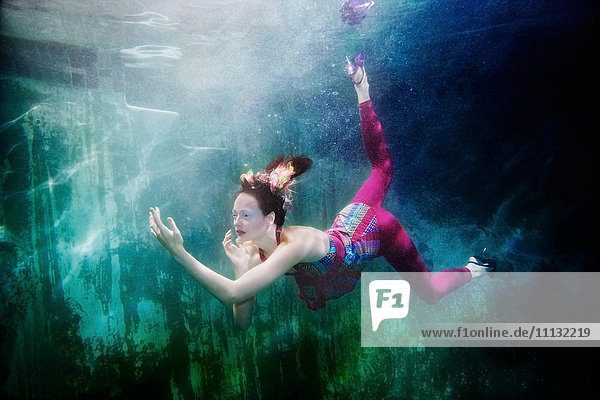 Kaukasische Frau in Kleidung schwimmt unter Wasser