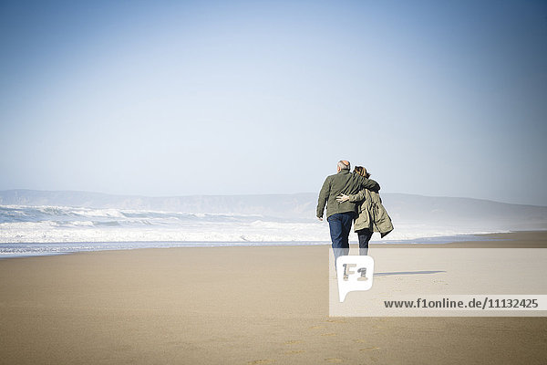 Kaukasisches Paar geht am Strand spazieren