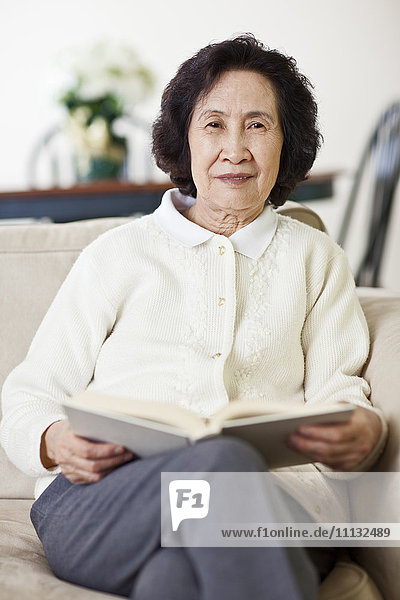 Chinesische Frau auf Sofa beim Lesen eines Buches