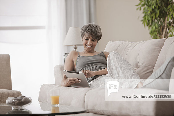 Gemischtrassige Frau auf Sofa mit digitalem Tablet