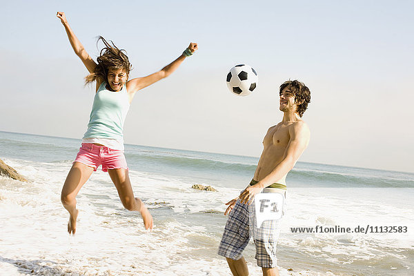 Pärchen spielt mit Fußball am Strand