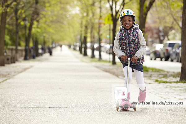 Gemischtrassiges Mädchen fährt auf einem Roller auf dem Bürgersteig