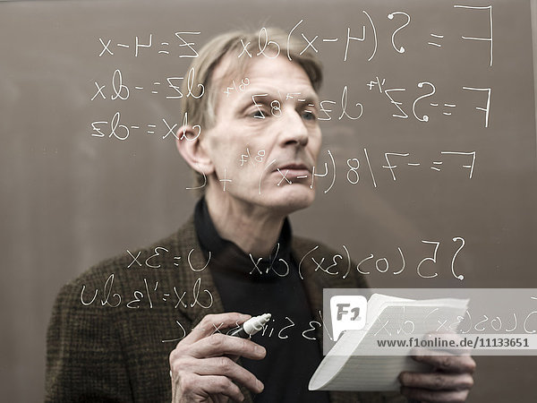 Caucasian teacher looking at formula on glass wall