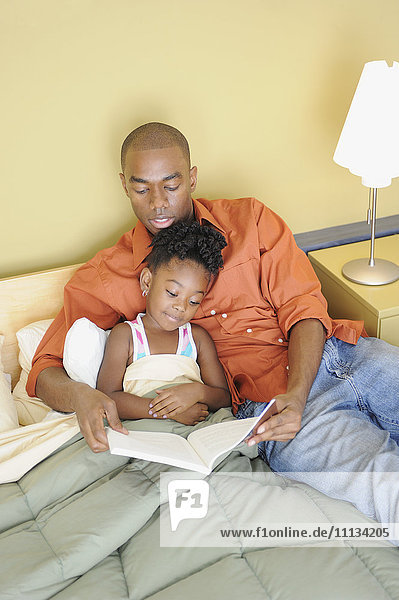 Schwarzer Vater liest seiner Tochter im Schlafzimmer ein Buch vor