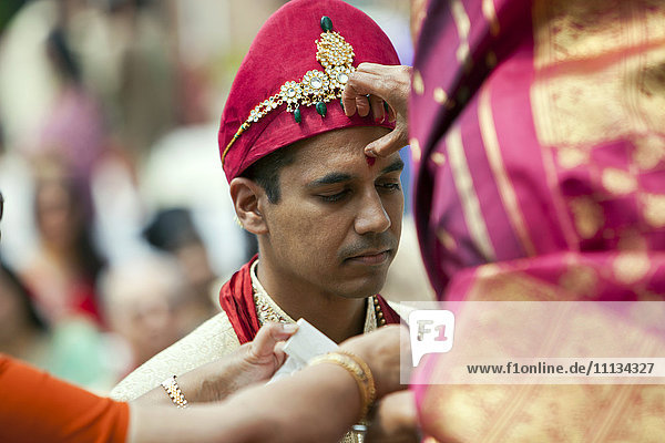Indische Frau markiert die Stirn des Bräutigams