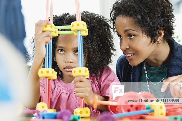 Afroamerikanisches Mädchen spielt mit Spielzeug  während die Mutter zusieht