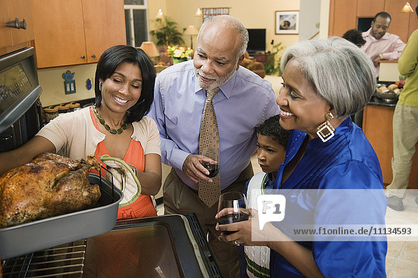 Afroamerikanische Familie sieht zu  wie eine Frau den Thanksgiving-Truthahn aus dem Ofen nimmt