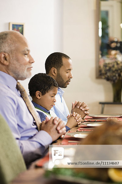 African American family saying grace at dinner table