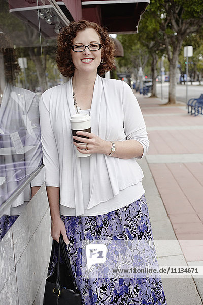 Mixed race woman drinking coffee on sidewalk