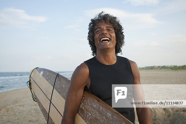 Gemischtrassiger Mann hält Surfbrett am Strand