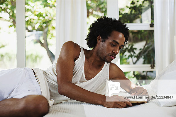 Mixed race man laying on bed reading