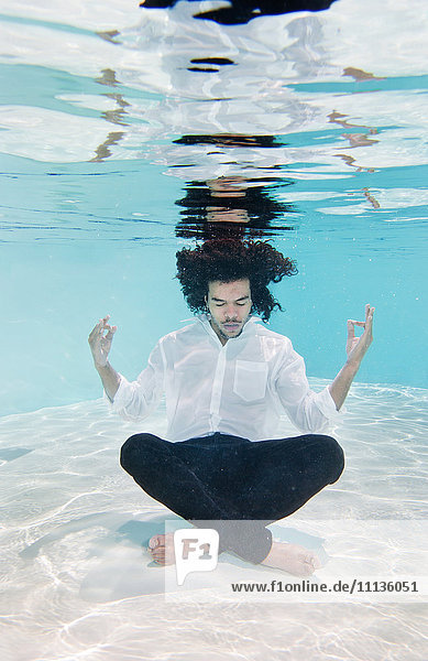 Gemischtrassiger Mann in Kleidung unter Wasser im Schwimmbad