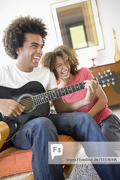 Frau lacht  während ihr Freund Gitarre spielt