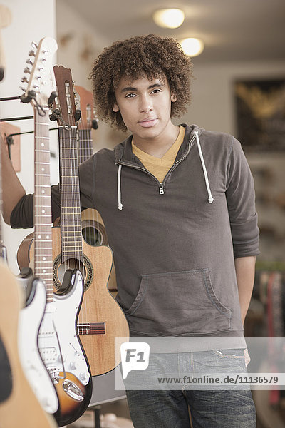 Mixed race teenager standing with guitars in music store