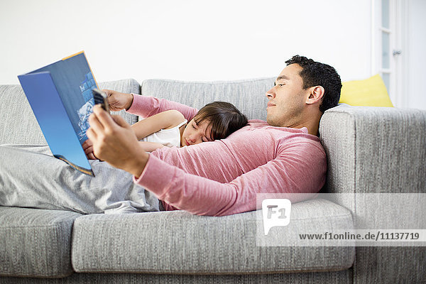 Vater und Tochter lesen gemeinsam auf dem Sofa
