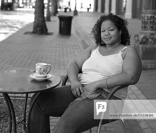 Gemischtrassige Frau trinkt Kaffee in einem Straßencafé