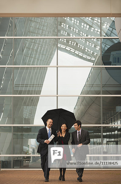 Geschäftsleute gehen zusammen mit Regenschirm