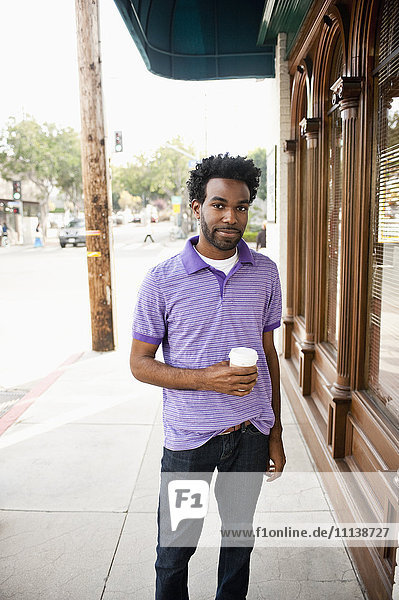 African American man with coffee cup standing on sidewalk