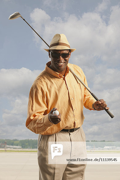 Afroamerikanischer Golfer mit Schläger und Ball auf dem Asphalt