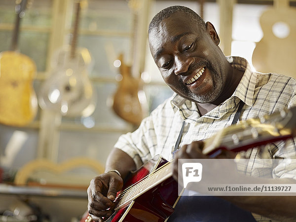 Black craftsman playing guitar in workshop