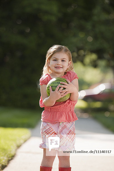 Kaukasisches Mädchen hält Wassermelone auf dem Gehweg