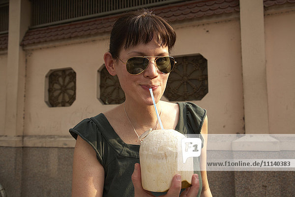 Gemischtrassige Frau trinkt aus einer Kokosnuss