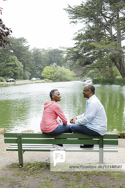 Afroamerikanisches Paar sitzt auf einer Bank in der Nähe eines Sees