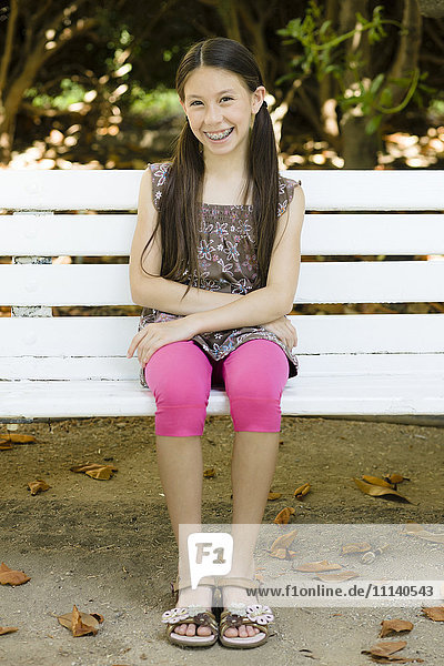 Lächelndes gemischtrassiges Mädchen sitzt auf einer Parkbank