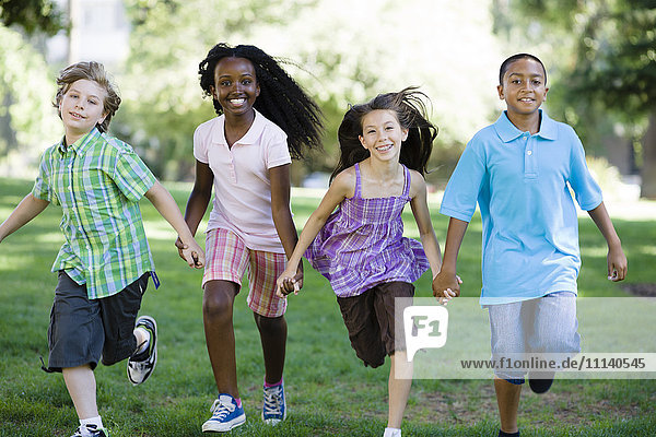 Glückliche Kinder halten sich an den Händen und laufen im Park