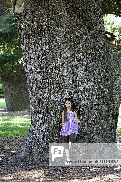 Gemischtrassiges Mädchen lehnt an einem Baumstamm im Park