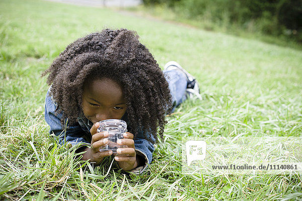 Afroamerikanischer Junge liegt im Gras und schaut in ein Glas