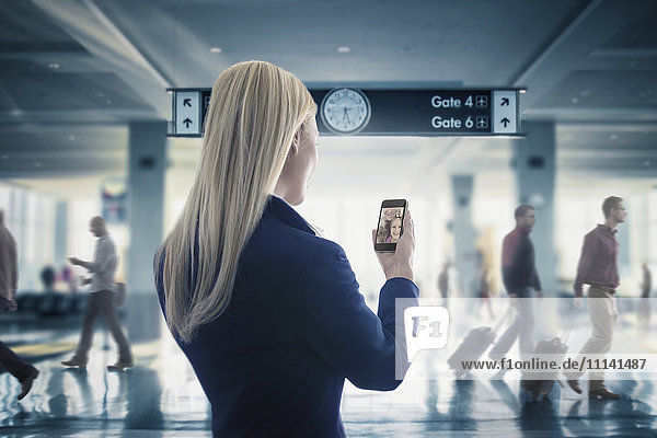 Kaukasische Geschäftsfrau  die im Flughafen eine Textnachricht auf ihrem Mobiltelefon schreibt