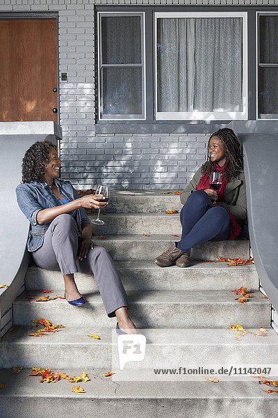Schwarze Mutter und Tochter sitzen auf der Treppe und trinken Wein